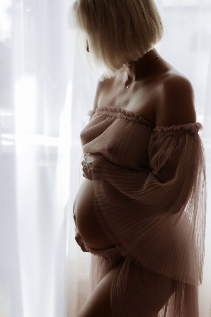 Babybauch-Silhouette im weichen Licht am Studiofenster